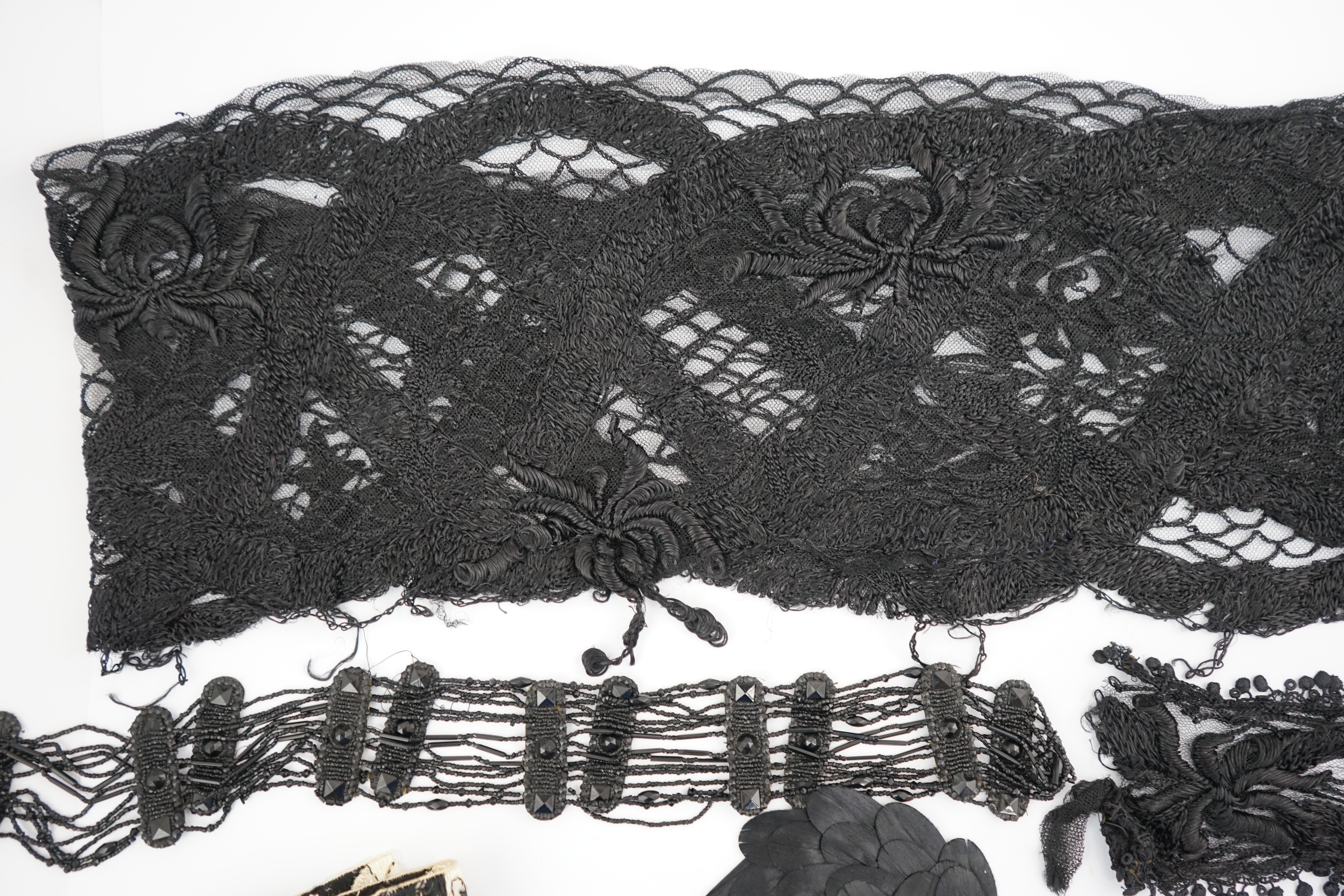 An 1930's black sequin cape, trimmings and lace, an Art Deco black sequin decorated cape on black net, an Edwardian jet beaded belt, a Spanish silk fall cap, three panels of black machine lace, a long length black and cr